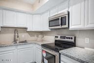 kitchen with light stone countertops, sink, white cabinets, and stainless steel appliances