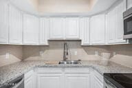 kitchen with light stone countertops, white cabinetry, and sink