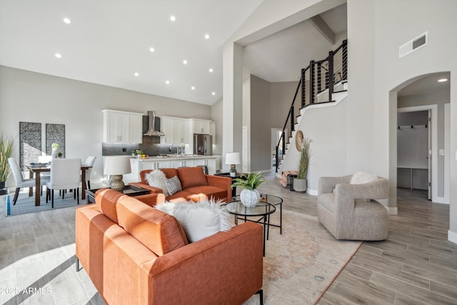 living room with a towering ceiling, sink, and light wood-type flooring