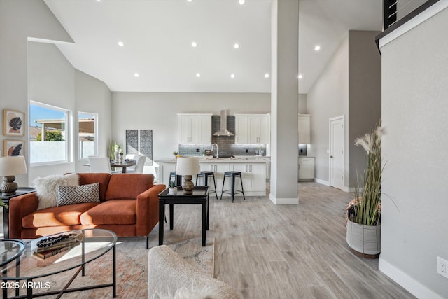 living room featuring high vaulted ceiling, sink, and light hardwood / wood-style flooring