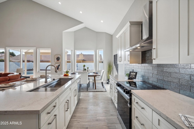 kitchen with wall chimney range hood, range with electric cooktop, sink, and white cabinets