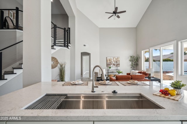 kitchen with ceiling fan, a towering ceiling, light stone countertops, and sink