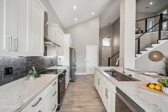 kitchen featuring wall chimney exhaust hood, sink, white cabinetry, appliances with stainless steel finishes, and light stone countertops