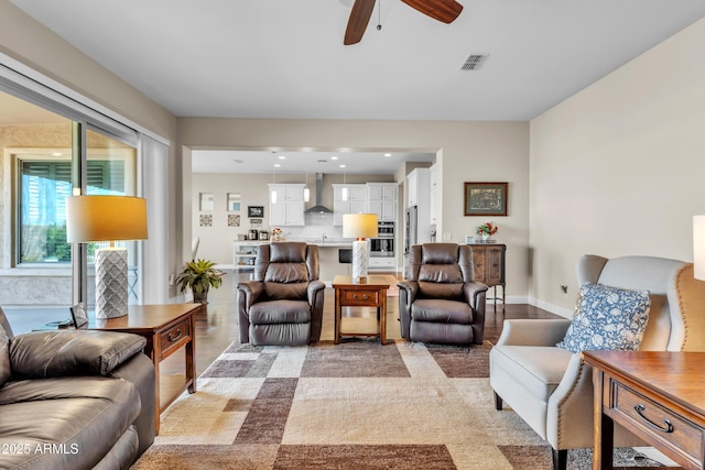 living room with baseboards, visible vents, and a ceiling fan