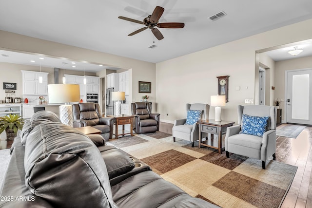 living area featuring light wood-type flooring, visible vents, ceiling fan, and baseboards