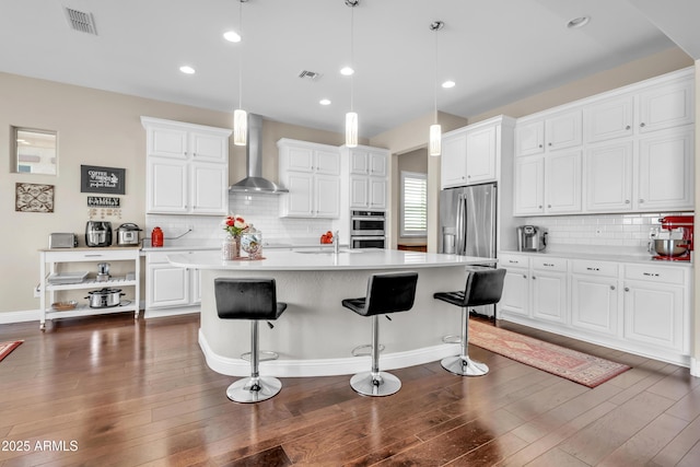 kitchen featuring dark wood-type flooring, visible vents, light countertops, wall chimney range hood, and appliances with stainless steel finishes