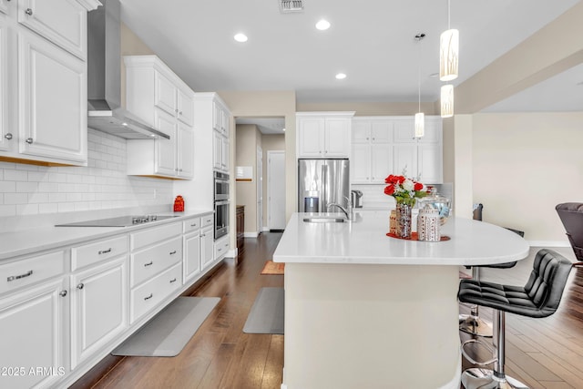 kitchen featuring a sink, a kitchen breakfast bar, appliances with stainless steel finishes, wall chimney exhaust hood, and dark wood finished floors