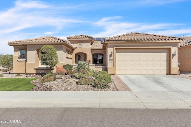 mediterranean / spanish-style home featuring a tile roof, stucco siding, concrete driveway, an attached garage, and roof mounted solar panels