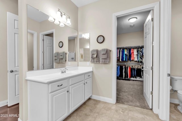 bathroom featuring baseboards, vanity, toilet, and a spacious closet