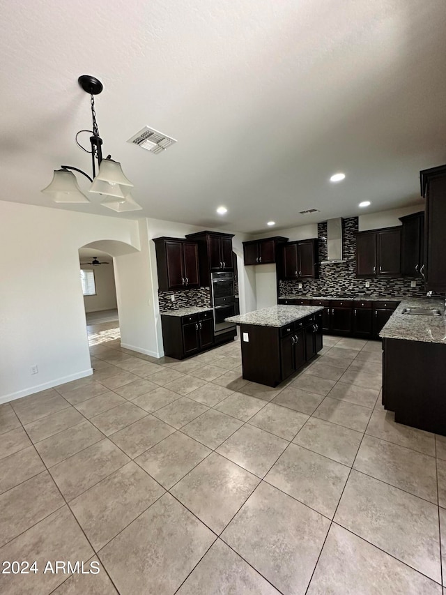 kitchen with a center island, backsplash, ceiling fan with notable chandelier, hanging light fixtures, and dark brown cabinetry