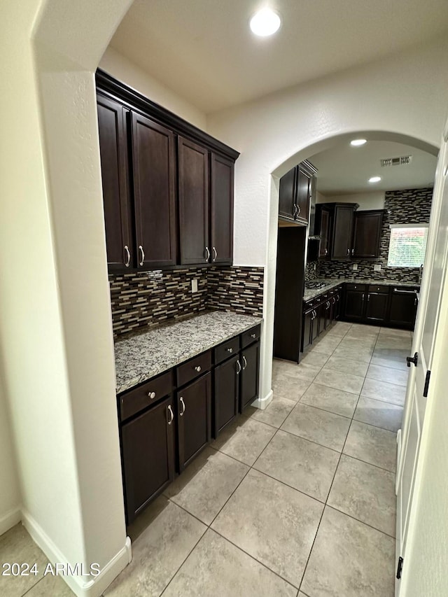 kitchen featuring light tile patterned floors, dark brown cabinetry, light stone counters, and backsplash