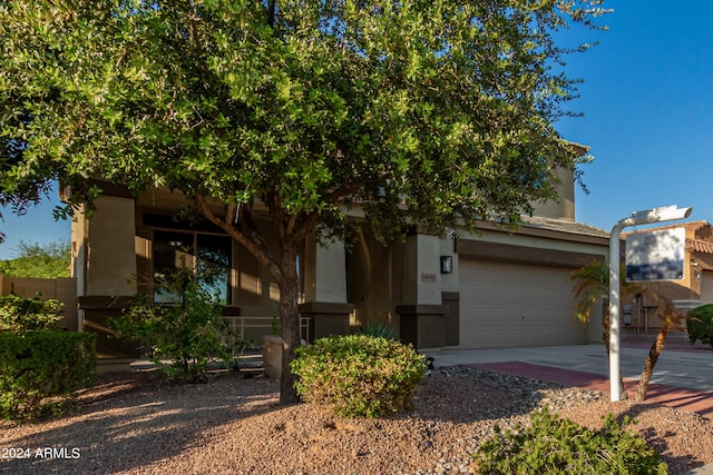 view of property hidden behind natural elements featuring concrete driveway, an attached garage, and stucco siding