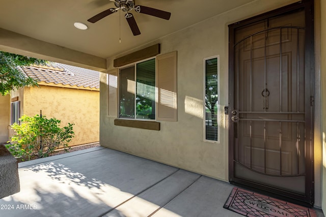 property entrance with stucco siding, a tiled roof, and a ceiling fan