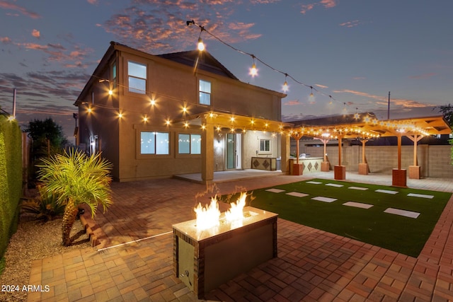 rear view of property featuring stucco siding, a patio, a fire pit, and fence