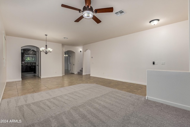 carpeted spare room with tile patterned flooring, ceiling fan with notable chandelier, visible vents, and arched walkways