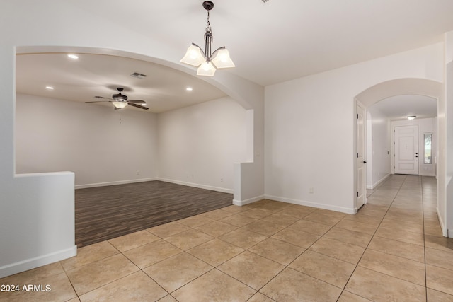 empty room with visible vents, baseboards, light tile patterned flooring, arched walkways, and ceiling fan with notable chandelier