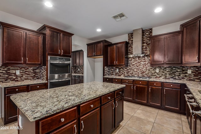 kitchen featuring wall chimney range hood, light stone countertops, visible vents, and stainless steel appliances