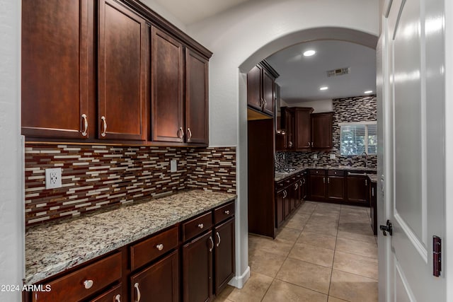 kitchen featuring tasteful backsplash, visible vents, light stone countertops, light tile patterned floors, and arched walkways