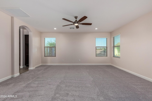 carpeted spare room featuring baseboards, arched walkways, visible vents, and a healthy amount of sunlight