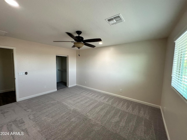 unfurnished bedroom with ceiling fan, a spacious closet, carpet floors, and a closet