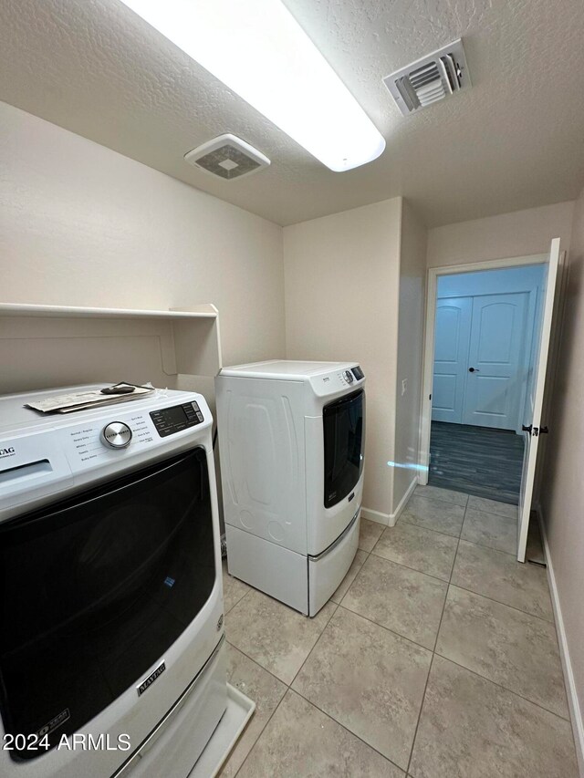 laundry area featuring light tile patterned flooring, a textured ceiling, and independent washer and dryer