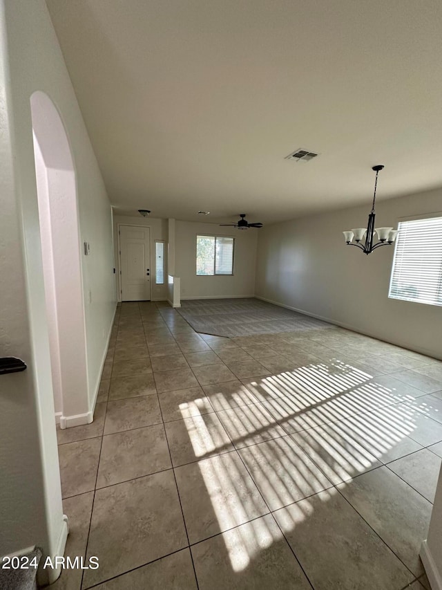 unfurnished living room featuring light tile patterned floors, ceiling fan with notable chandelier, and a healthy amount of sunlight