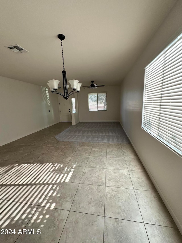 unfurnished dining area with light tile patterned flooring and ceiling fan with notable chandelier