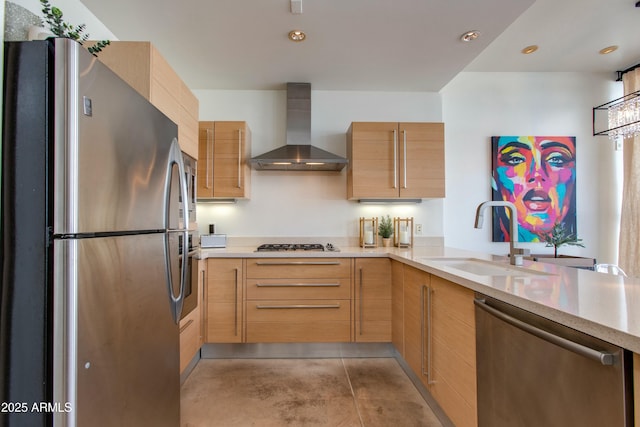 kitchen featuring stainless steel appliances, wall chimney range hood, a sink, light brown cabinets, and recessed lighting