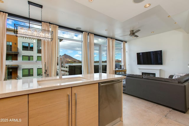 kitchen with a sink, light brown cabinets, a chandelier, open floor plan, and a glass covered fireplace