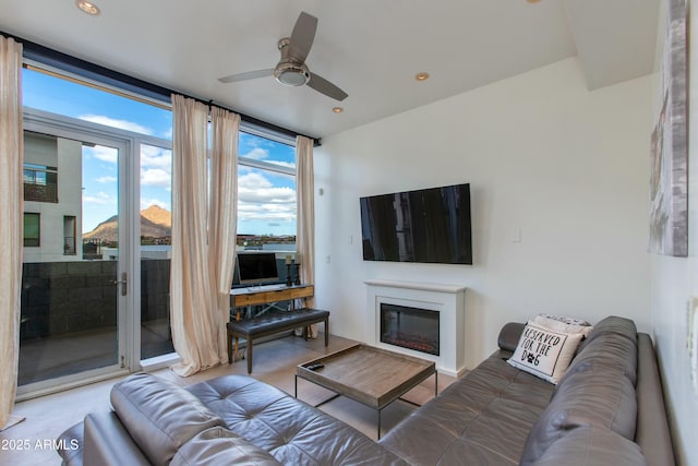 living area with ceiling fan, a glass covered fireplace, and recessed lighting