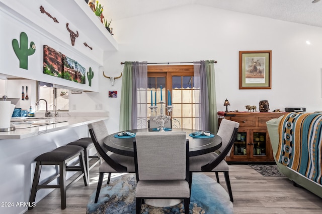 dining space with light hardwood / wood-style flooring, lofted ceiling, and sink