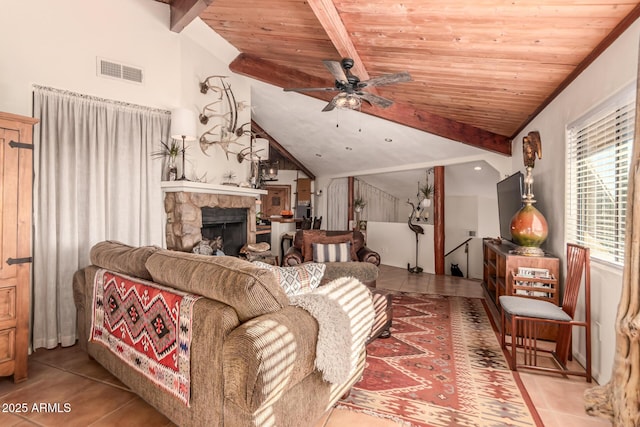 tiled living room with ceiling fan, wooden ceiling, lofted ceiling with beams, and a stone fireplace