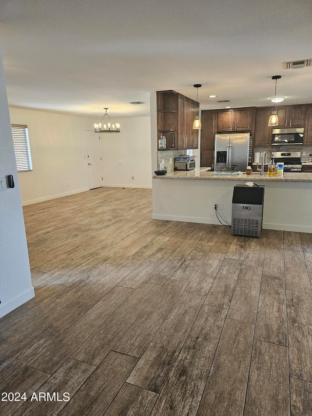 kitchen with appliances with stainless steel finishes, light stone counters, dark brown cabinetry, pendant lighting, and dark hardwood / wood-style floors