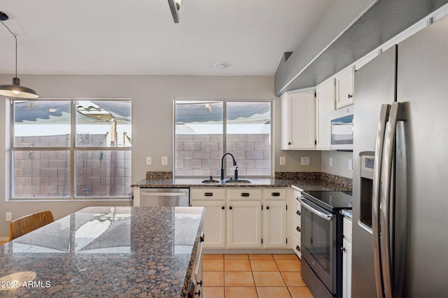 kitchen featuring light tile patterned flooring, white cabinets, a sink, decorative light fixtures, and stainless steel appliances