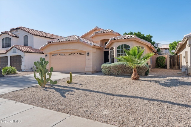 mediterranean / spanish house with fence, stucco siding, a tiled roof, concrete driveway, and an attached garage