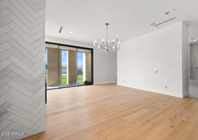 spare room featuring a notable chandelier, baseboards, and light wood-style floors