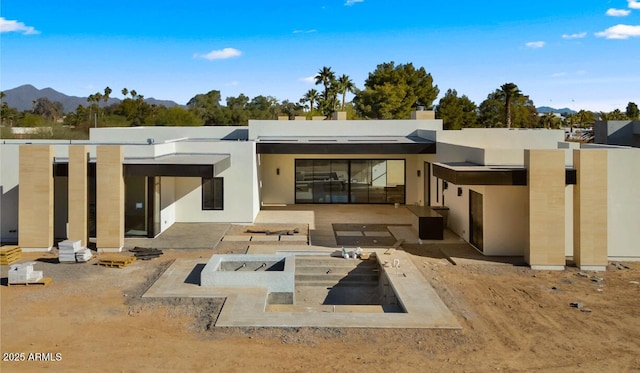 rear view of property with a patio area, stucco siding, a mountain view, and a fire pit