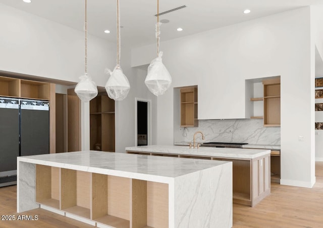 kitchen featuring open shelves, backsplash, a large island with sink, and light wood finished floors