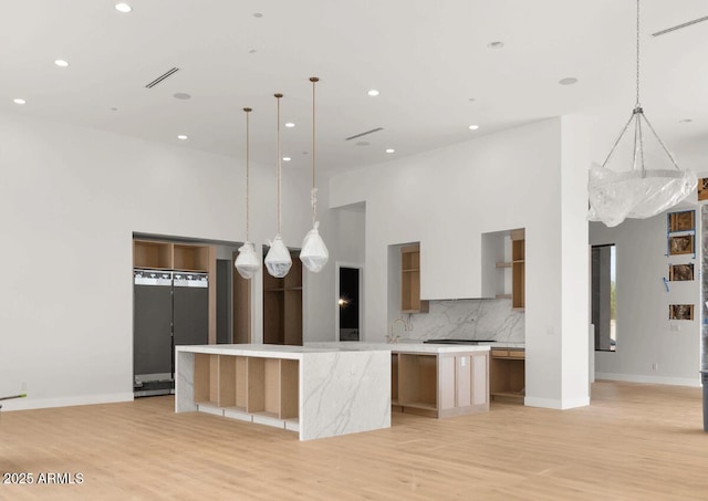 kitchen featuring backsplash, modern cabinets, a large island with sink, and a towering ceiling