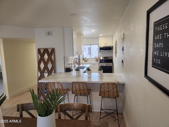 kitchen featuring baseboards, appliances with stainless steel finishes, white cabinetry, a textured wall, and light wood-type flooring