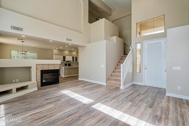 unfurnished living room with beam ceiling, a tiled fireplace, light hardwood / wood-style flooring, and high vaulted ceiling