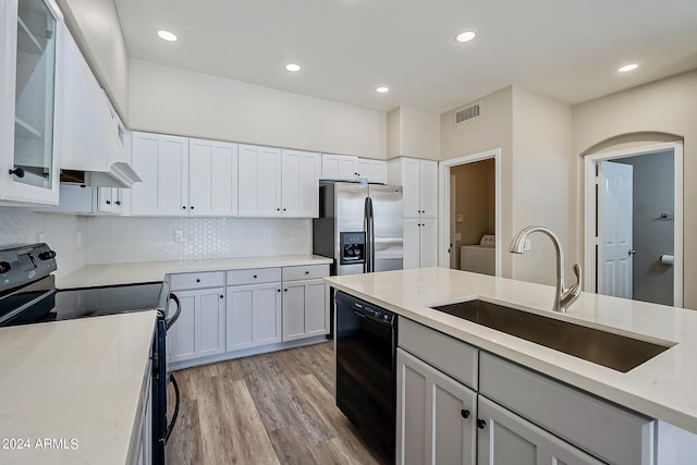 kitchen featuring a sink, visible vents, light wood-style floors, black appliances, and washer / clothes dryer