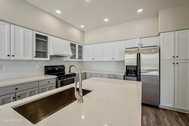 kitchen featuring light stone counters, custom exhaust hood, stainless steel appliances, tasteful backsplash, and glass insert cabinets