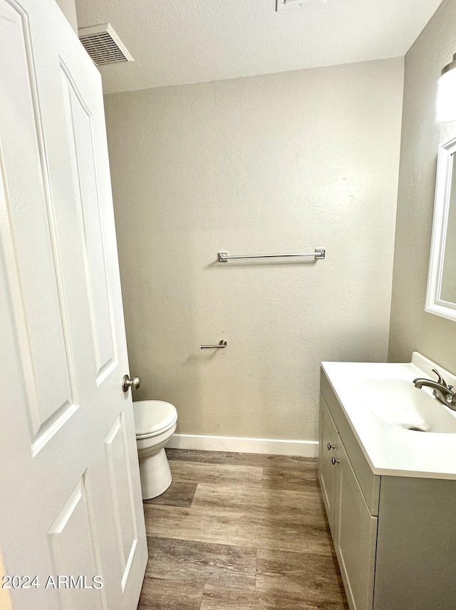 half bath featuring visible vents, toilet, vanity, wood finished floors, and baseboards