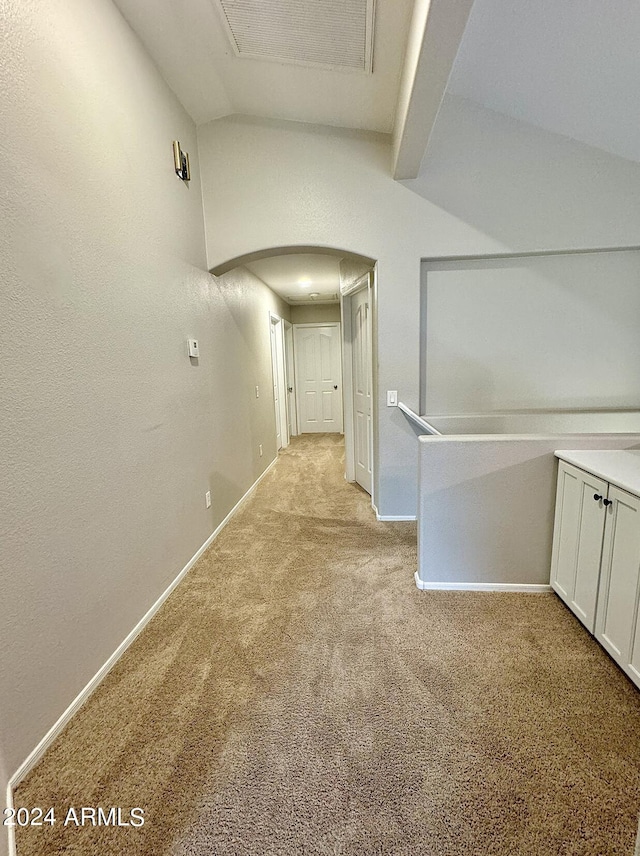 hall with arched walkways, light colored carpet, visible vents, vaulted ceiling, and baseboards