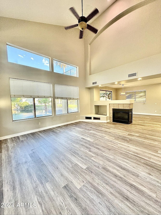 unfurnished living room featuring a tiled fireplace, ceiling fan, hardwood / wood-style flooring, and a healthy amount of sunlight