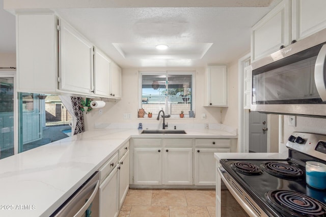 kitchen featuring sink, appliances with stainless steel finishes, light stone counters, a tray ceiling, and white cabinets