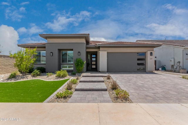 prairie-style home featuring a garage, decorative driveway, a front lawn, and stucco siding