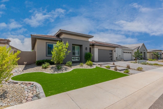 prairie-style house with an attached garage, fence, driveway, stucco siding, and a front yard