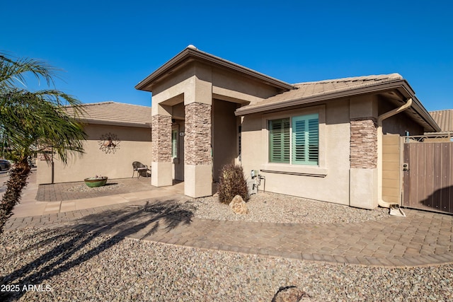 rear view of property with stone siding, a patio area, a gate, and stucco siding